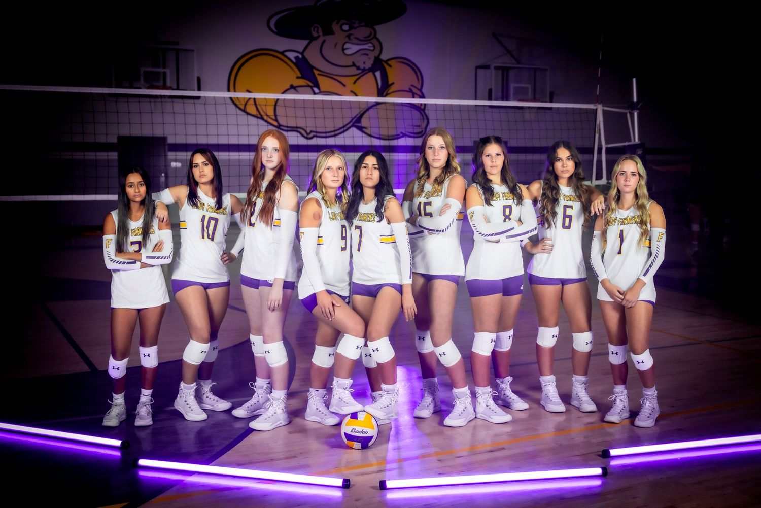 Volleyball team poses on court with purple LED lighting and mascot logo in background.