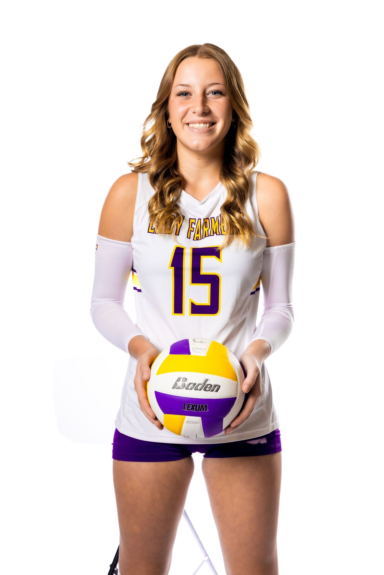 Volleyball athlete in white jersey holds purple and yellow ball for team photo.