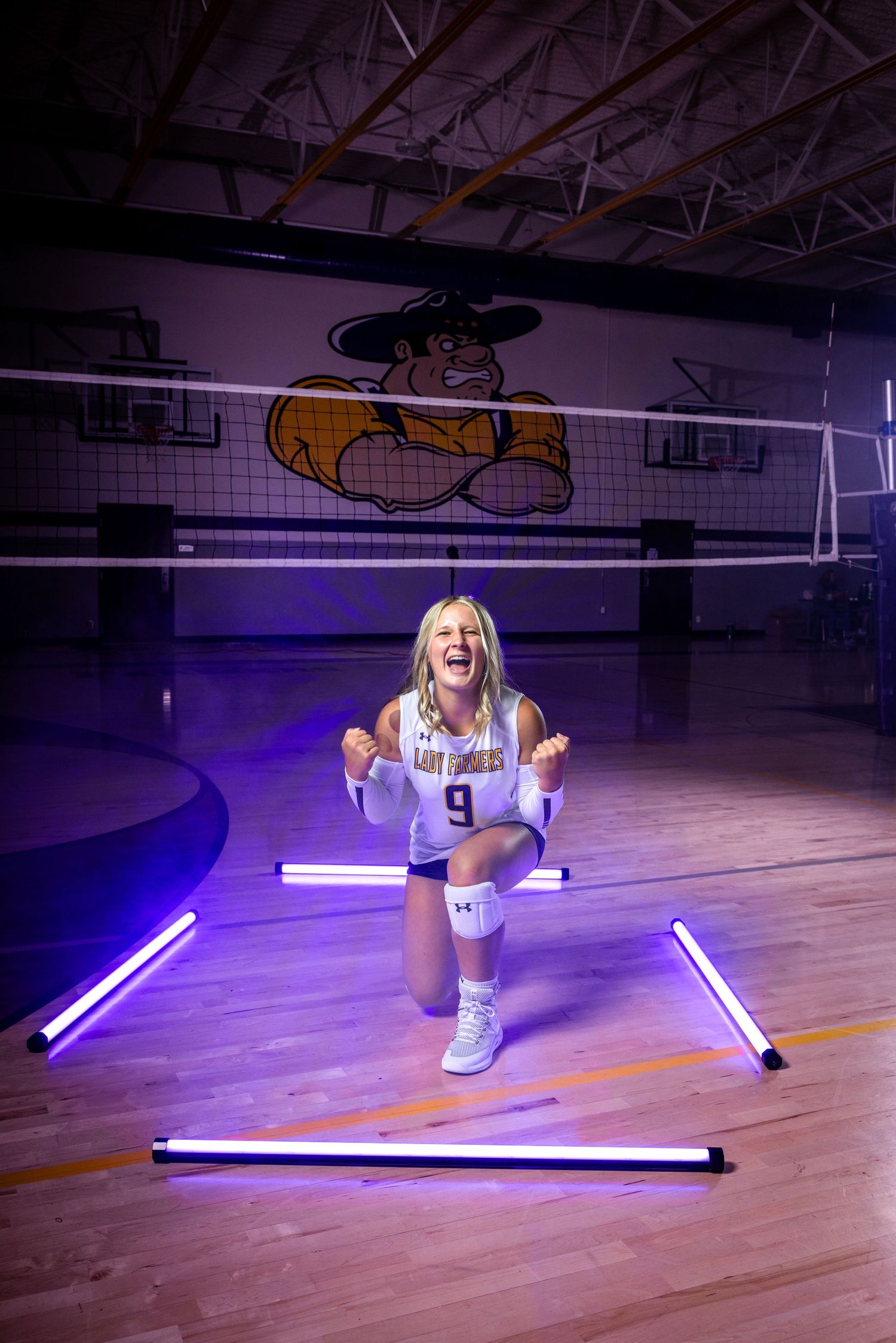 Athlete poses in gym with purple LED lights and school mascot logo visible on wall.