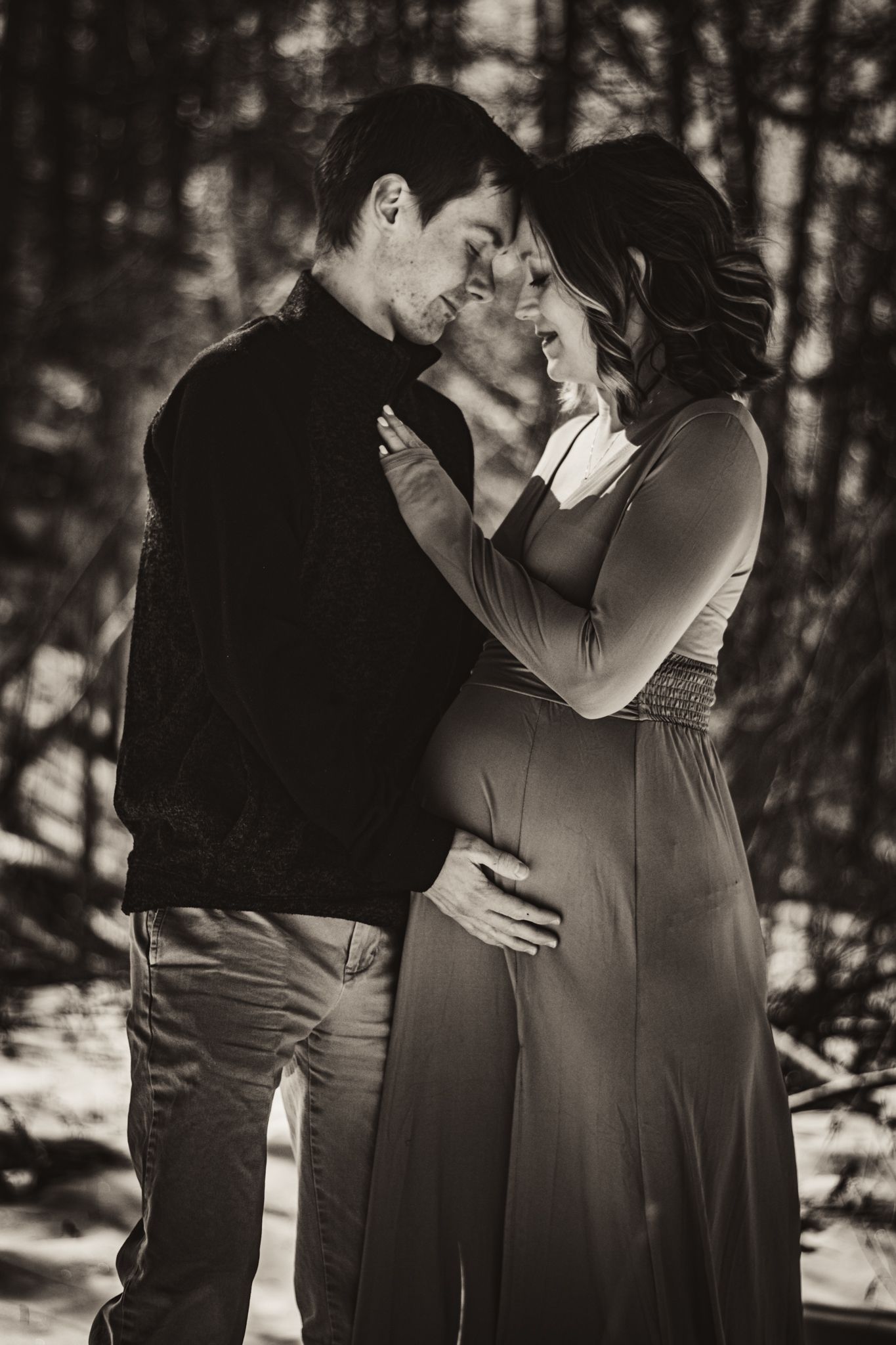 A black and white portrait of a couple embracing during their maternity session in the snow.