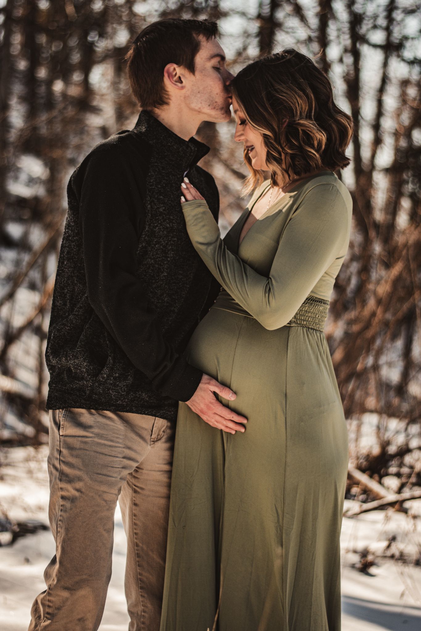 A couple embraces during an intimate winter maternity photo session in the woods.