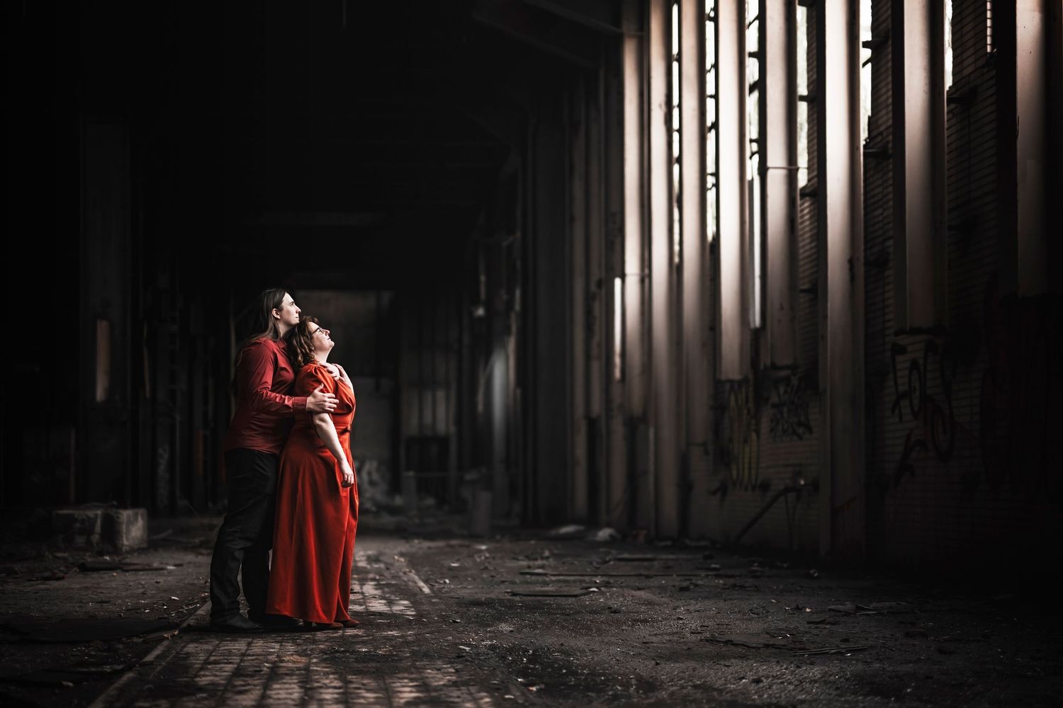 Romantic couple in dramatic lighting embrace in an abandoned industrial space.