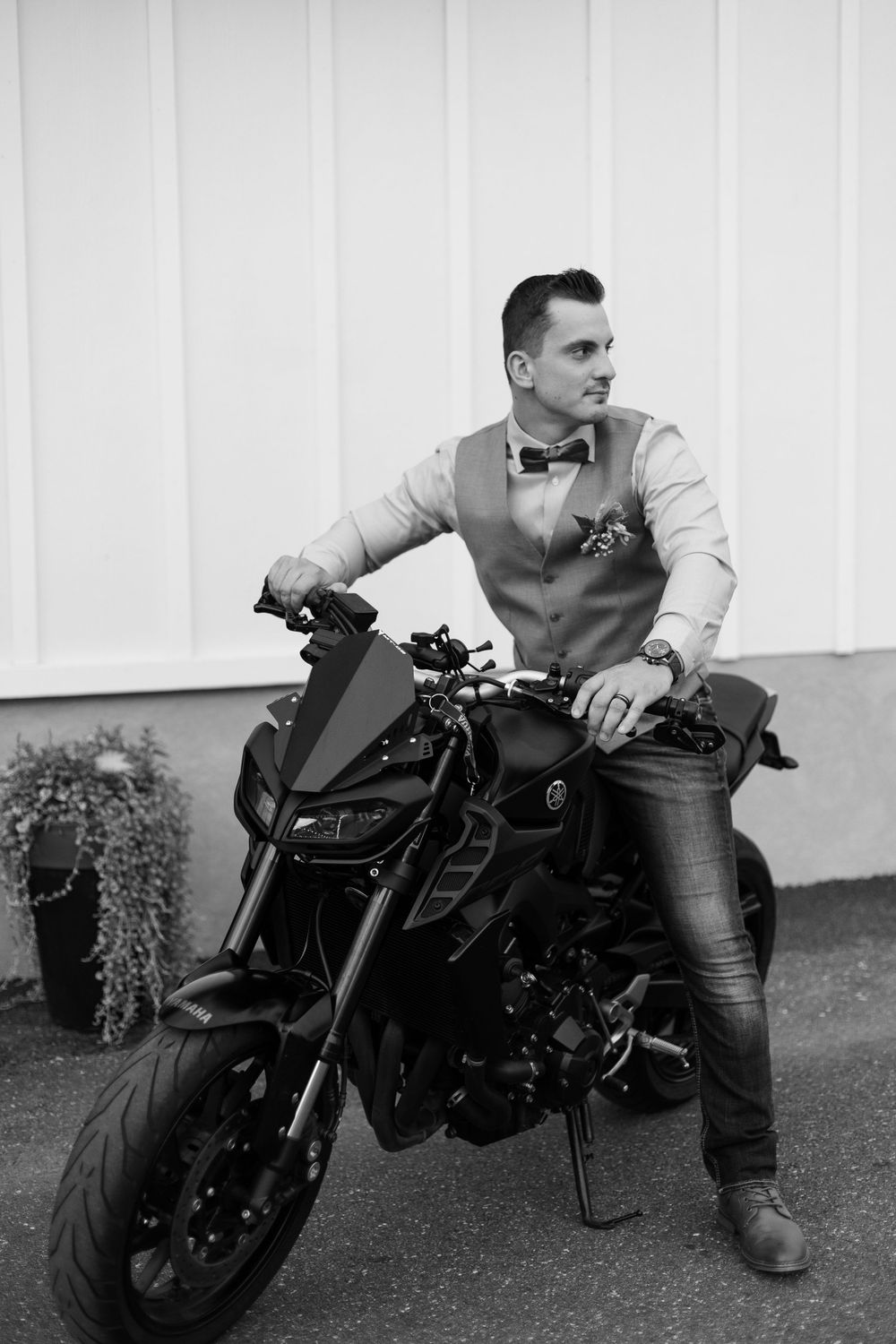 Black motorcycle parked against white wall with formal attire rider.