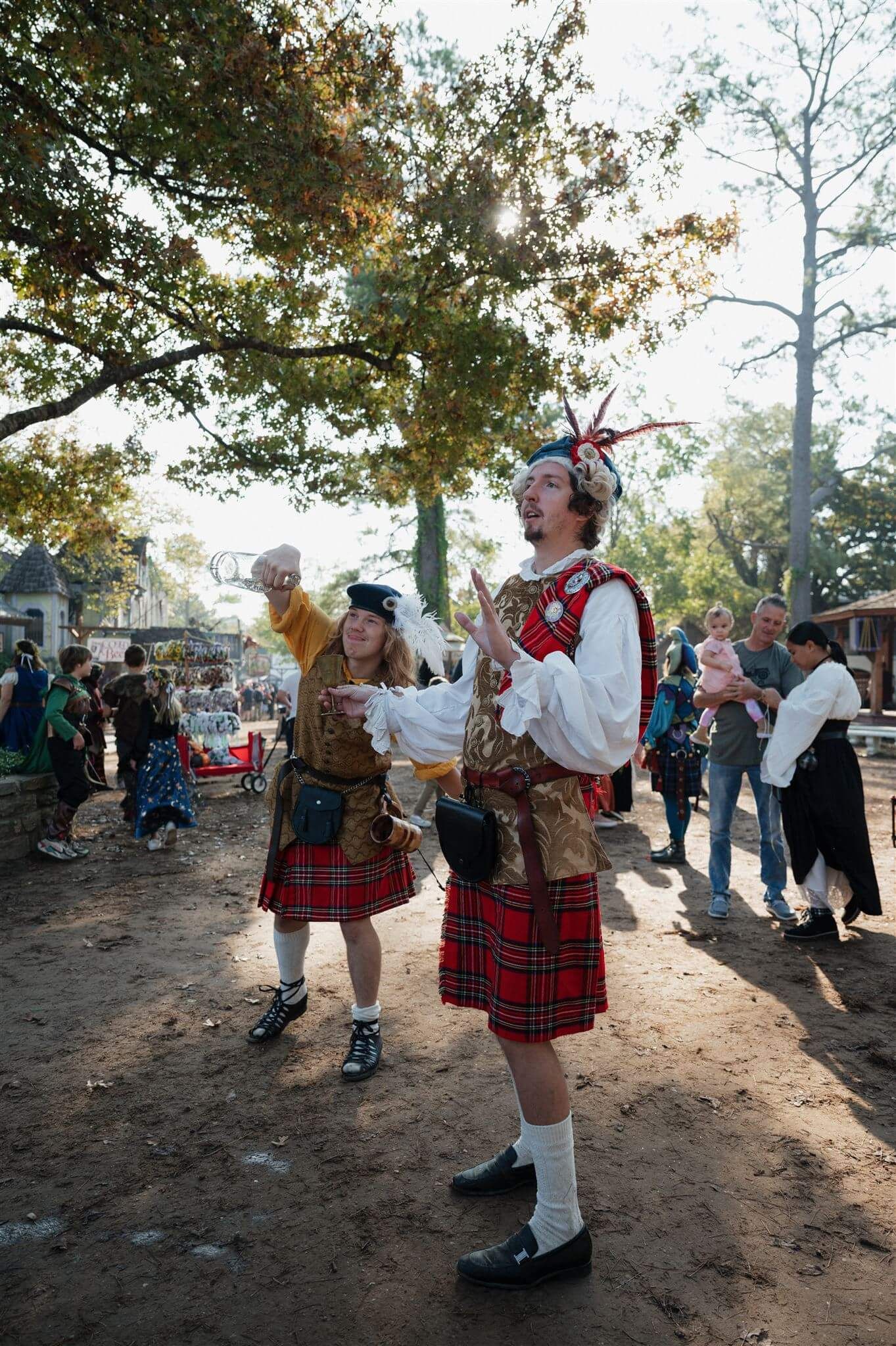 Performers in kilts and traditional Scottish attire at an outdoor renaissance festival.
