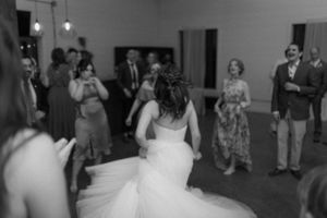 black and white image of a bride twirling and dancing at her reception surrounded by loved ones