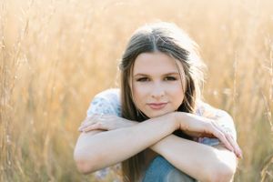 facial shot of a louisiana senior in a field on tall golden grass. her hands are rested on knee and her chin on hands