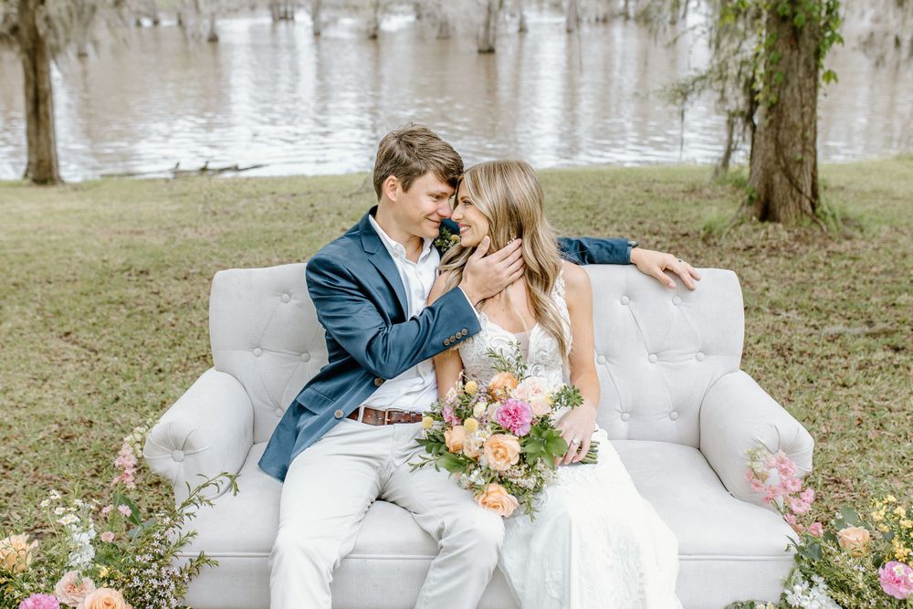 bride and groom sitting with faces close on a couch surrounded by flowers