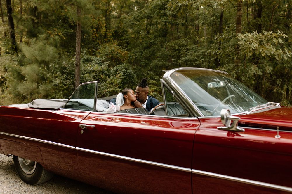 bride and groom kissing in the backseat of a candy apple red classic convertible car