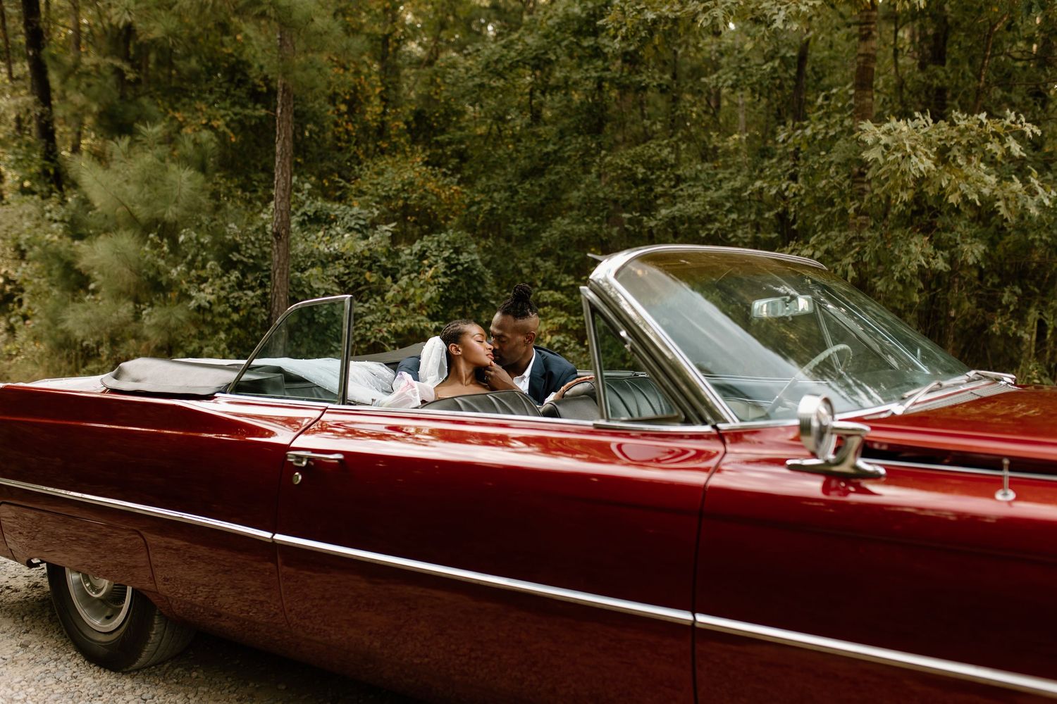 bride and groom kissing in the backseat of a candy apple red classic convertible car