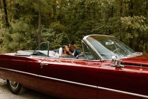 bride and groom kissing in the backseat of a candy apple red classic convertible car