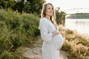 pregnant momma on the banks of a louisiana river bank surrounded by tall flowy grass with a bridge in background