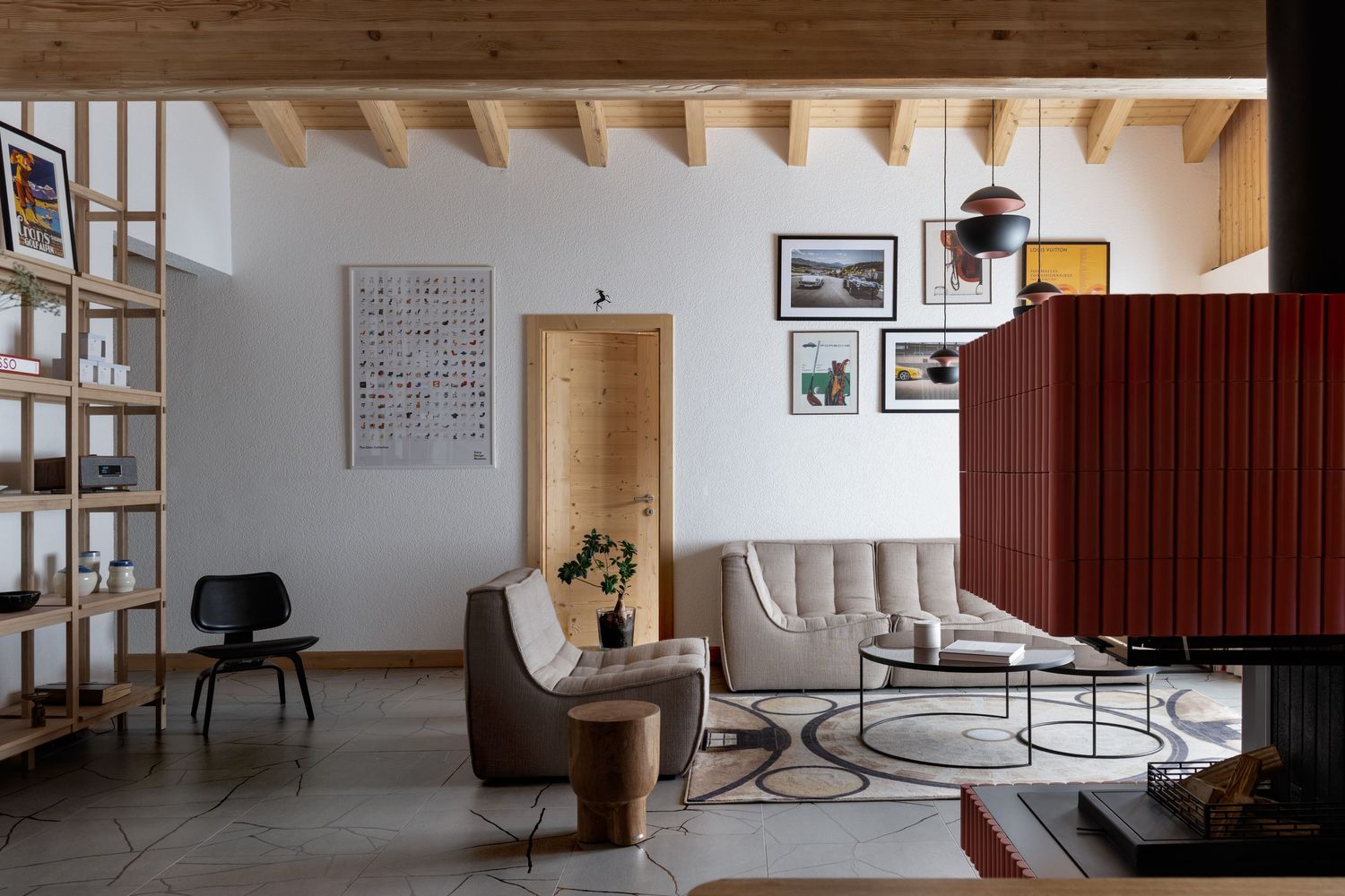 A living room with wooden bookshelves and ceilings beams as well as red heating oven.