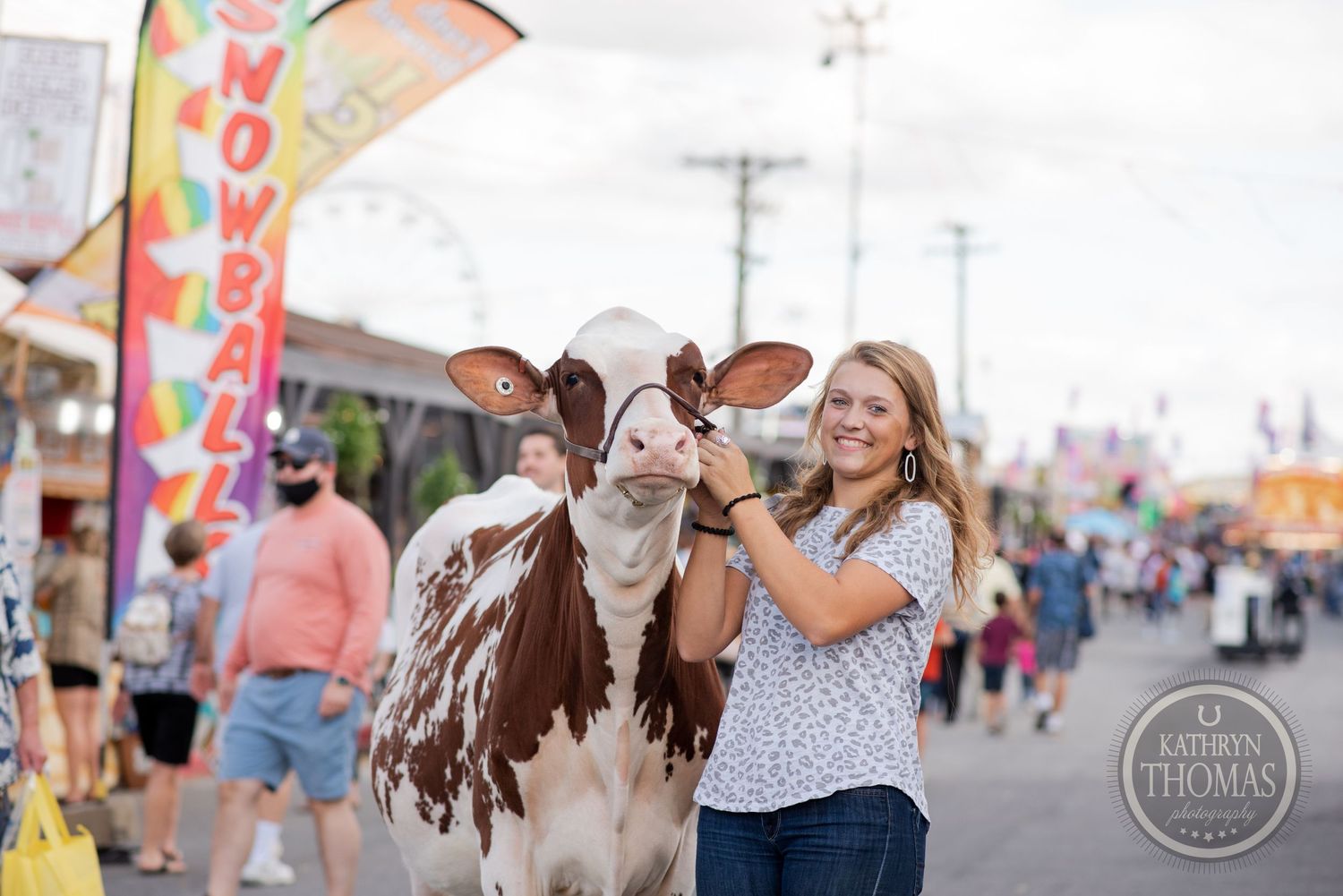 A dairy cow receives affection from its handler at a lively fair with colorful flags.