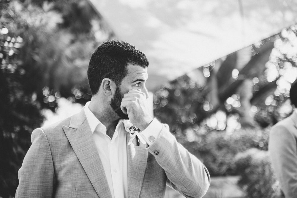 Emotional groom wipes tears during outdoor wedding ceremony in black and white.
