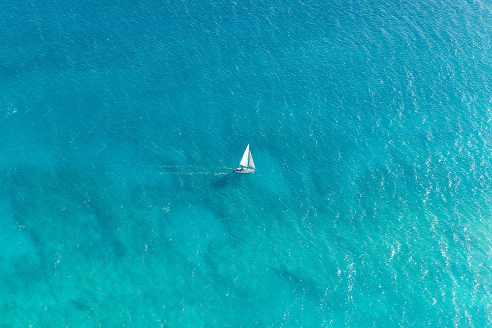 Aerial view of a lone sailboat in crystal clear turquoise waters.