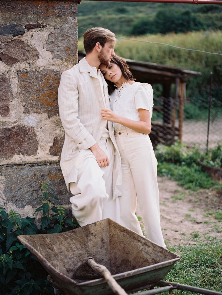A couple standing in the countryside in cream coloured outfits.