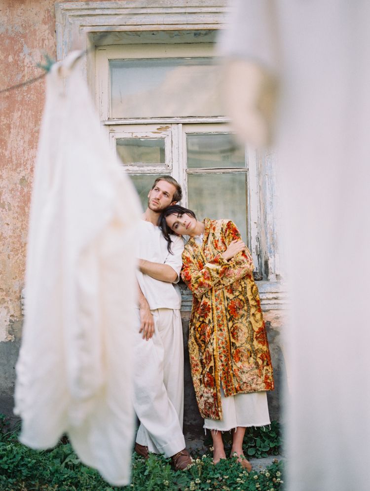 Shown through hanging laundry, a couple leans against the wall of their village home in Kazbegi.