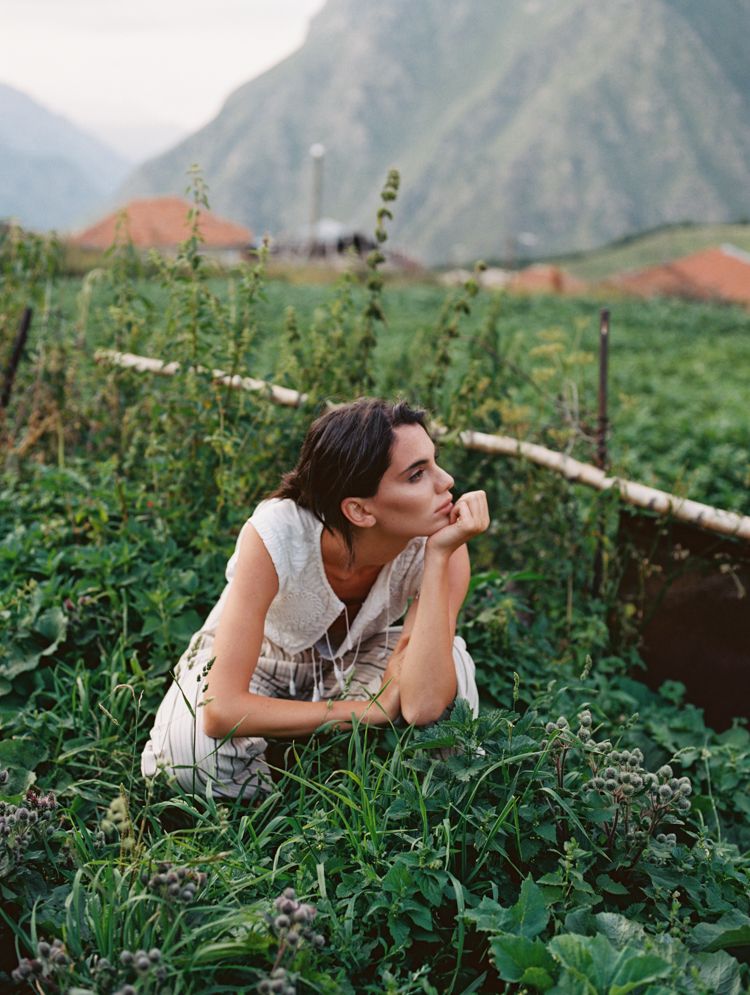 A model crouching down in a vegetable patch with the Caucasus mountains showing in the back.