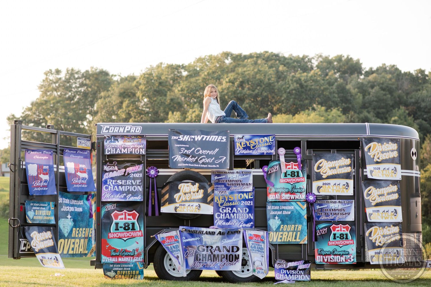 Show trailer displaying colorful banners and signs arranged in rows outdoors during golden hour sunlight.