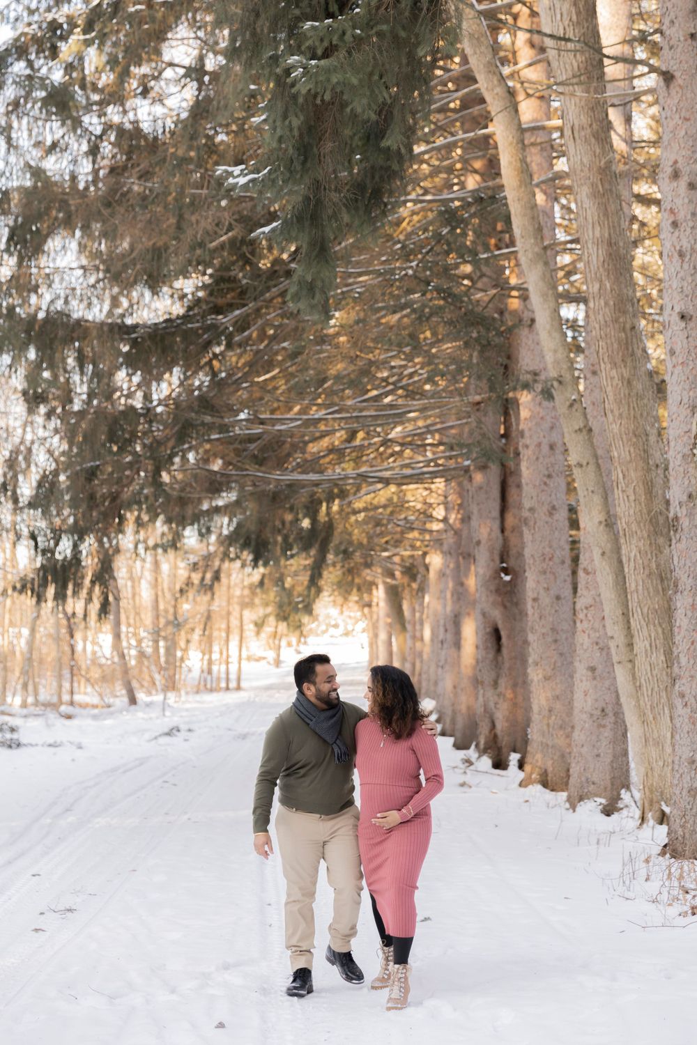 pregnant couple walking in the evergreen trees by Sheldon estates at stoney creek metropark