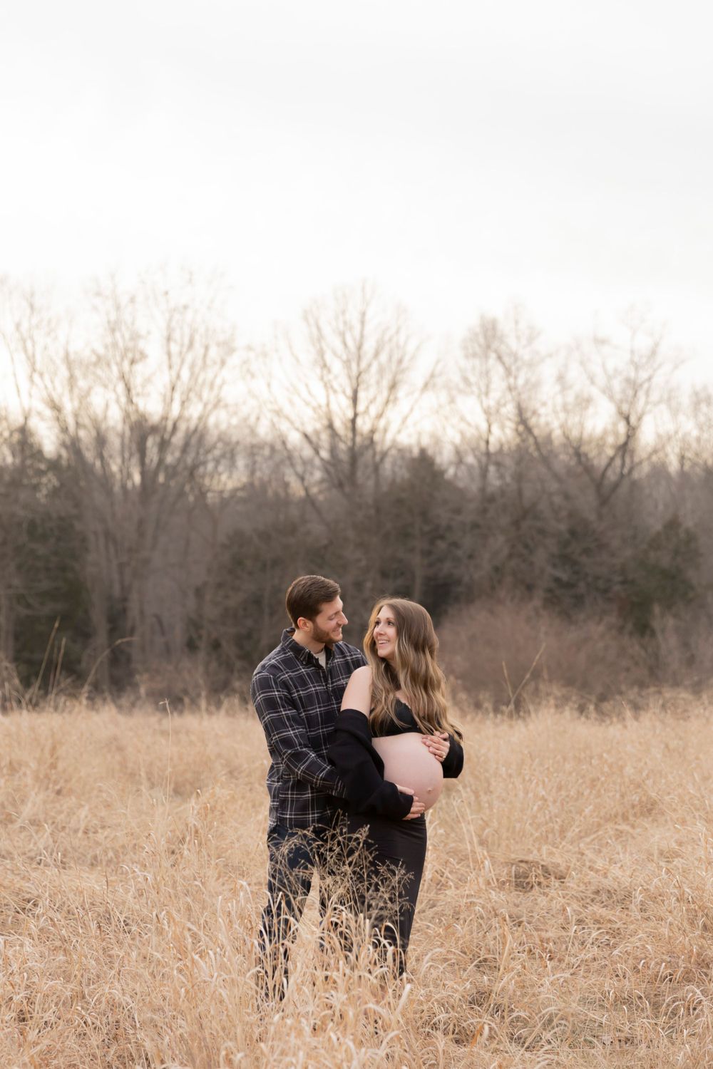 pregnant couple leaning against each other in the grasses by Sheldon estates at Stoney Creek metropark