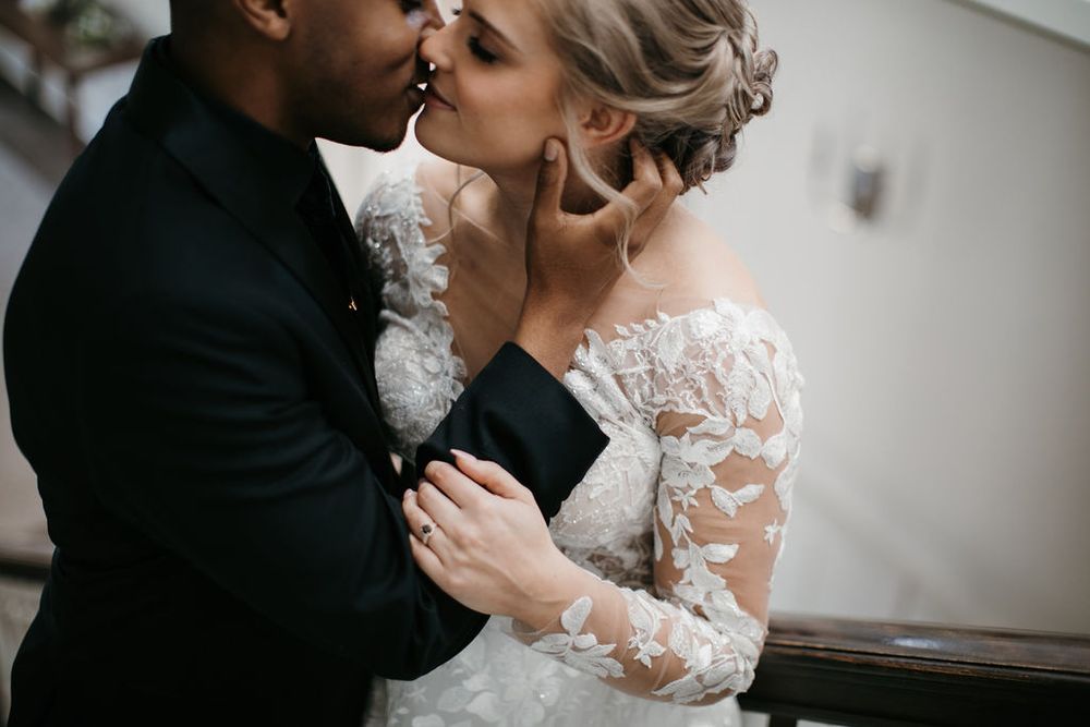 Close-up of interracial couple sharing tender kiss, bride in off-shoulder lace wedding gown.