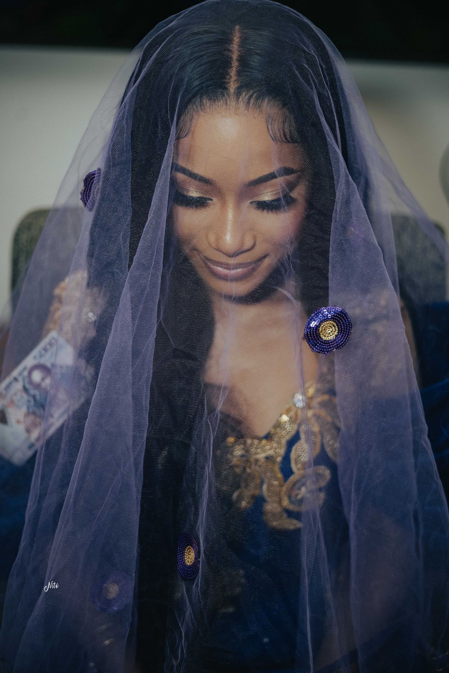 Close-up portrait under a purple veil with delicate gold embellishments and floral accents.