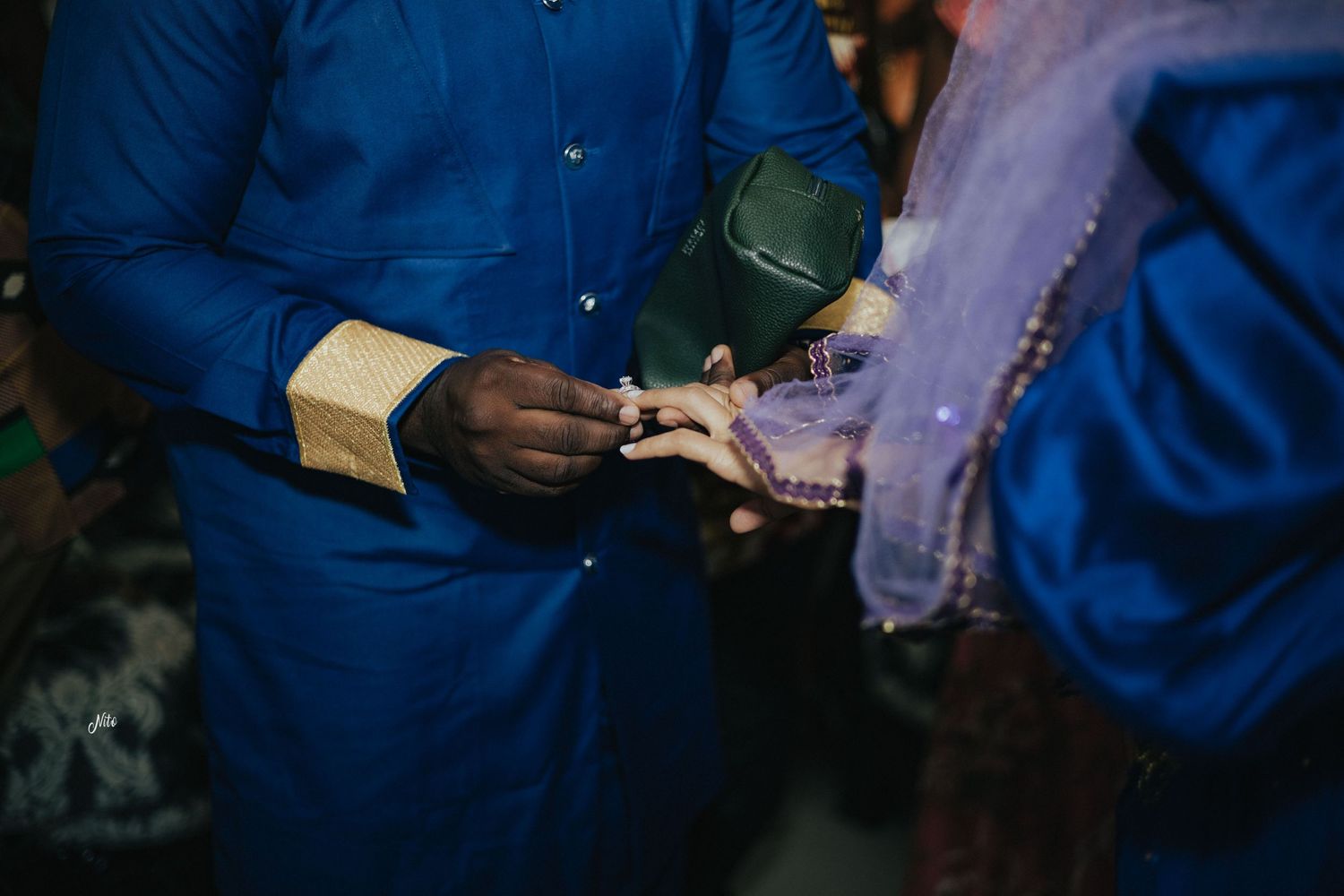 Close-up of hands during ring exchange ceremony with blue traditional attire visible.