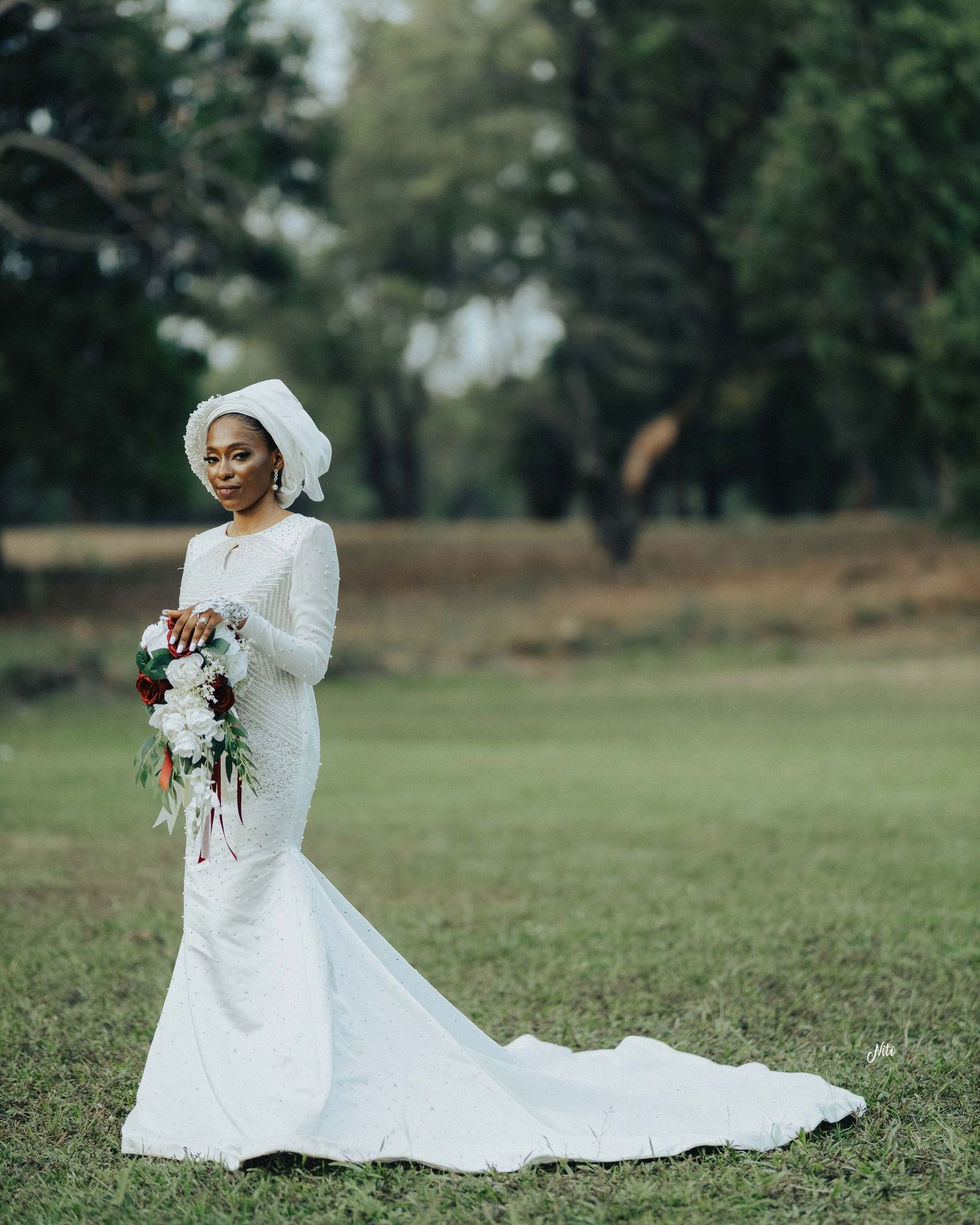 A bride in a fitted white gown with long sleeves poses with her bouquet in a garden setting.