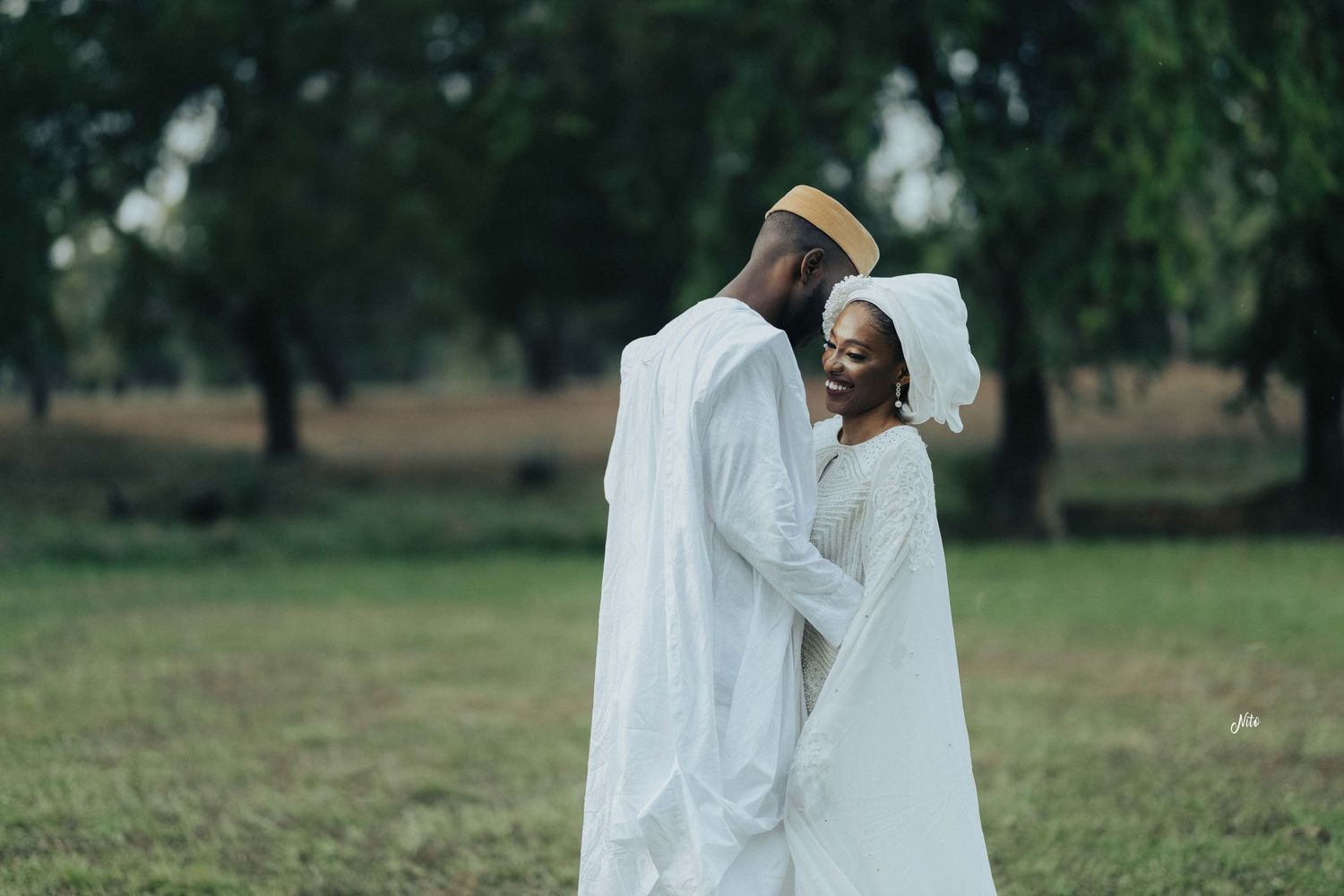 A tender embrace between two people wearing flowing white garments in a grassy field.