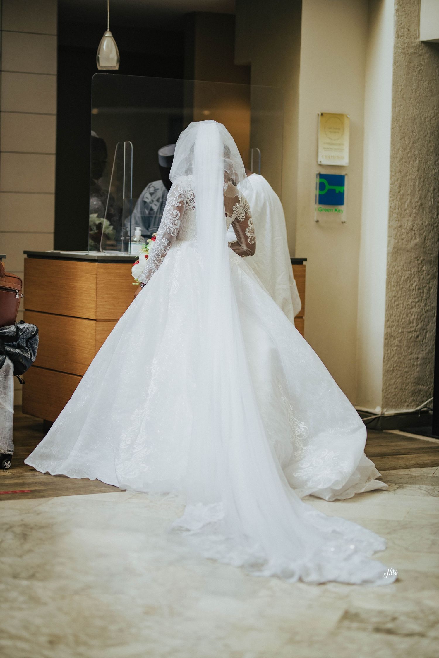 Back view of a wedding dress with intricate lace details and flowing train in an indoor setting.