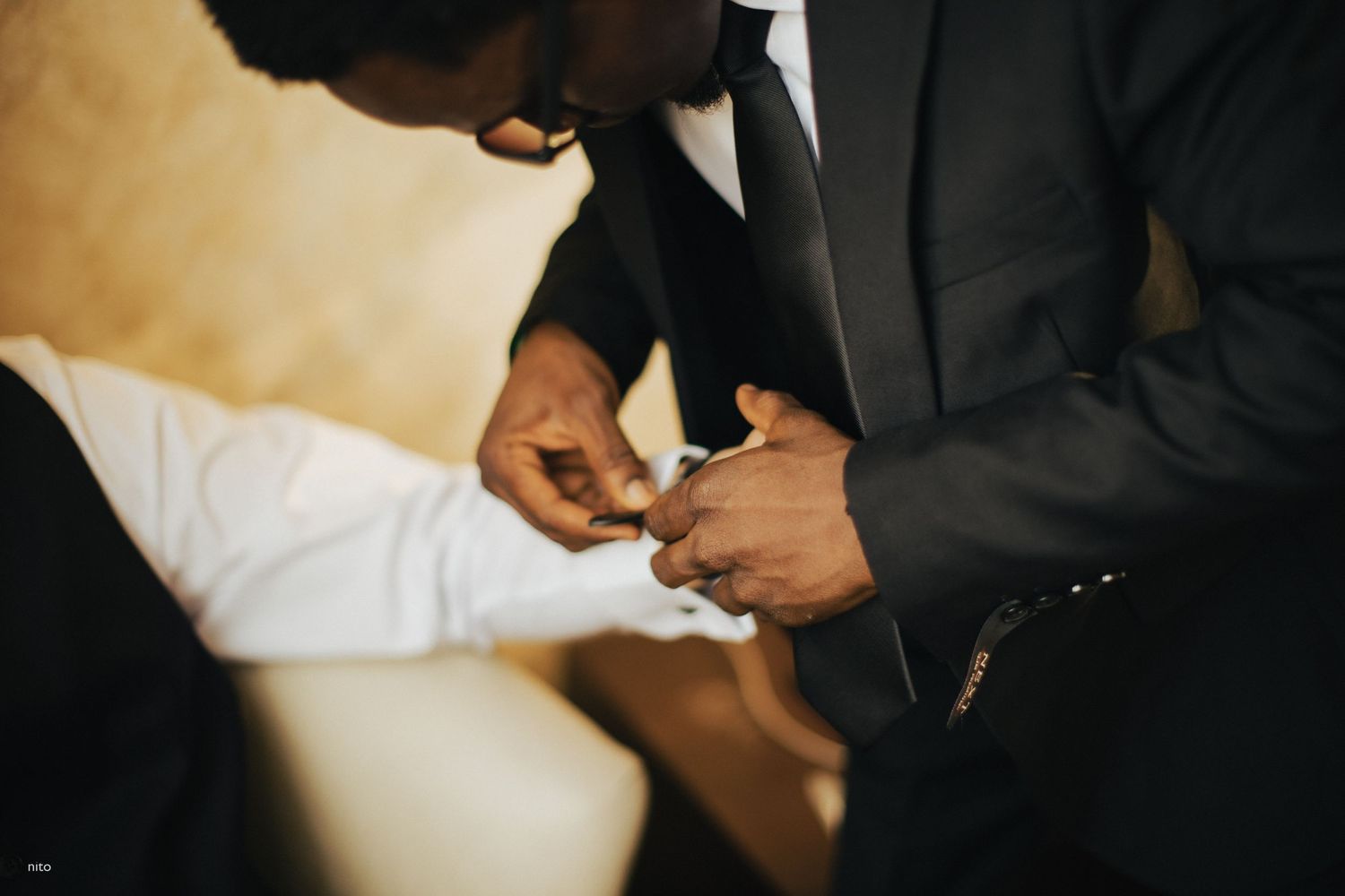 Close-up shot of hands adjusting formal attire in warm lighting.