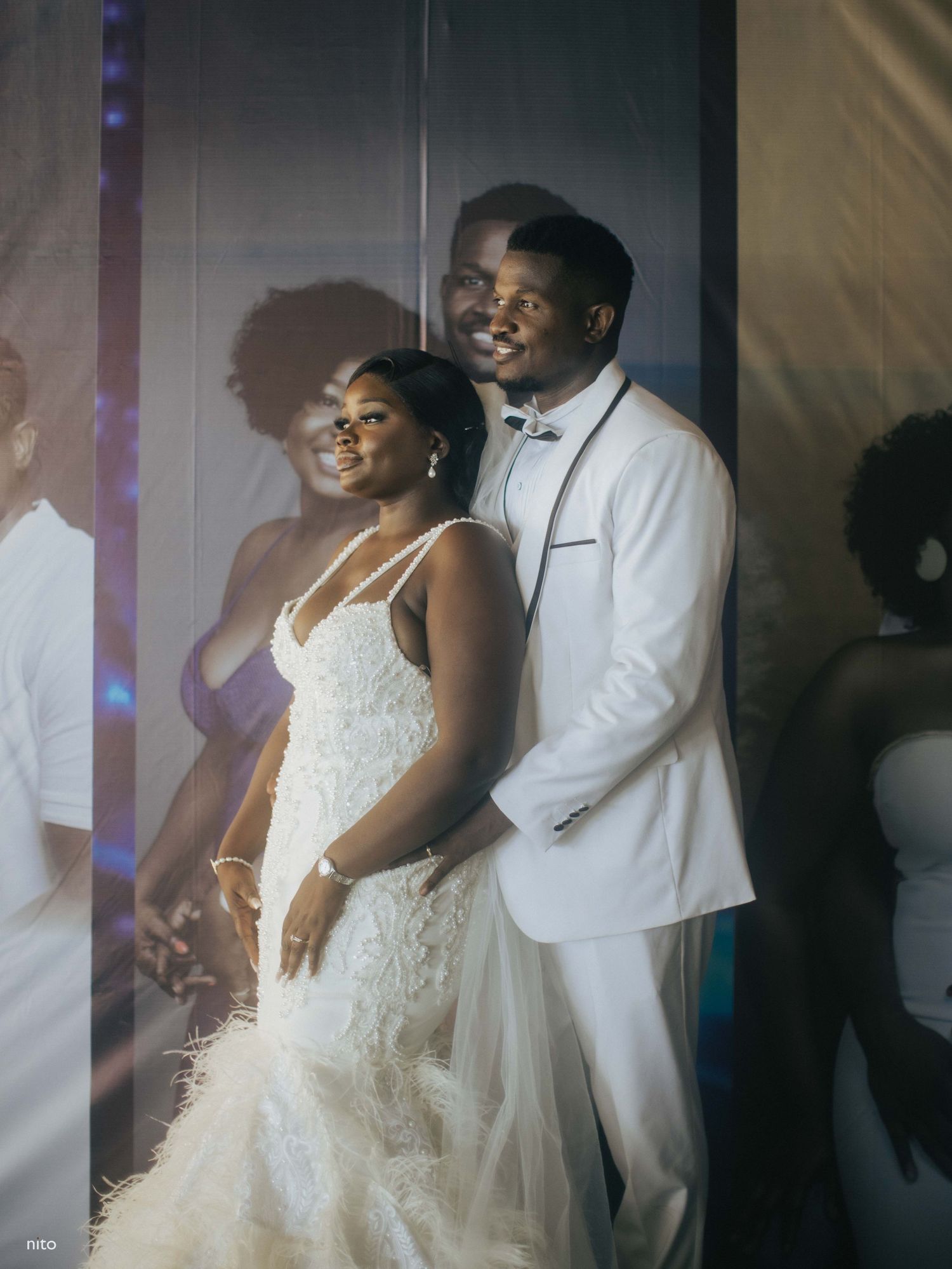 Newlyweds in white formal attire posing together under atmospheric lighting.
