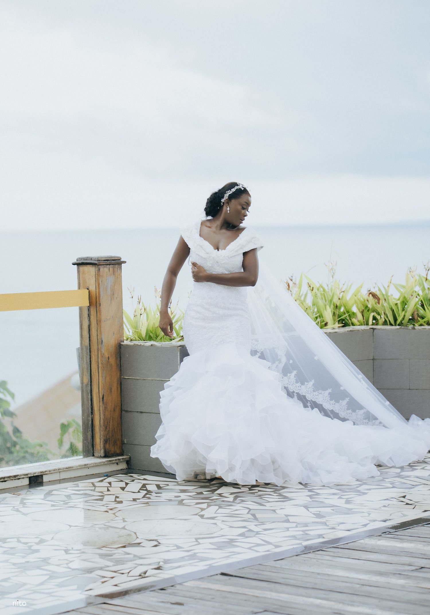 A stunning mermaid-style wedding gown captured on an outdoor deck with ocean views.