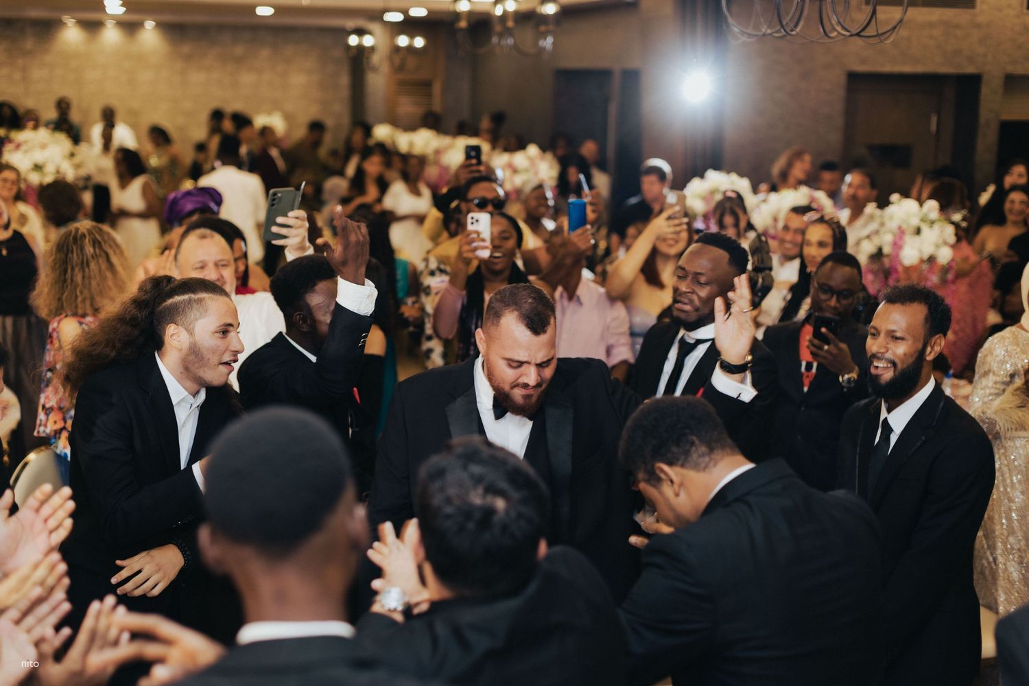 A celebratory moment during a wedding reception with guests cheering in a dimly lit venue.