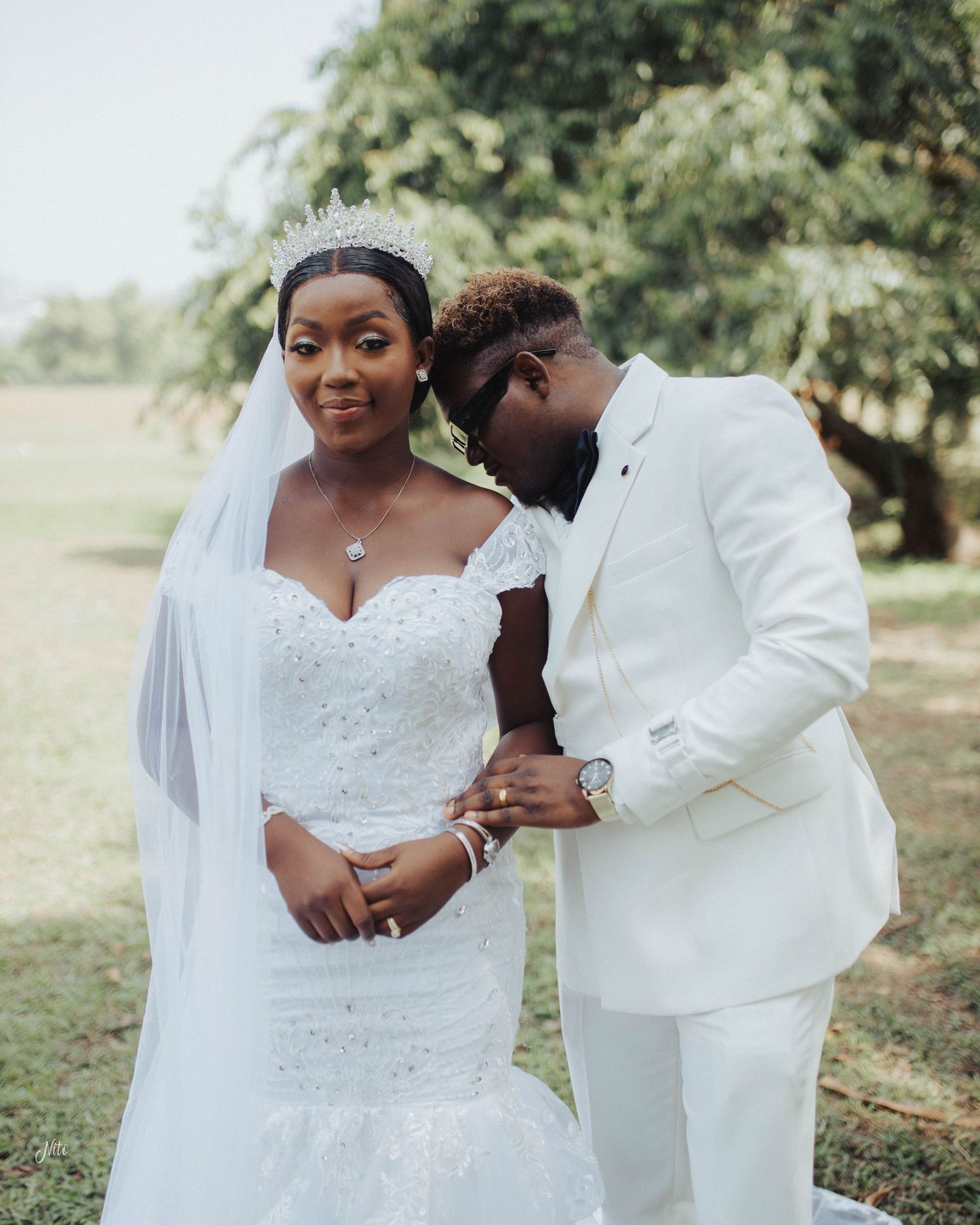 A newlywed couple shares a tender moment outdoors in their elegant white wedding attire.