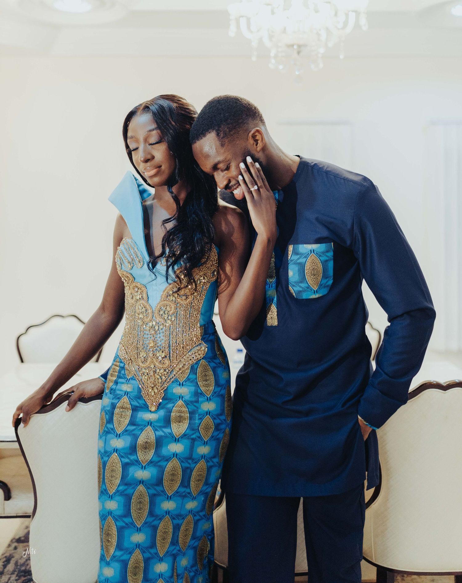 Couple sharing an intimate moment wearing coordinated blue and gold traditional African-inspired outfits.