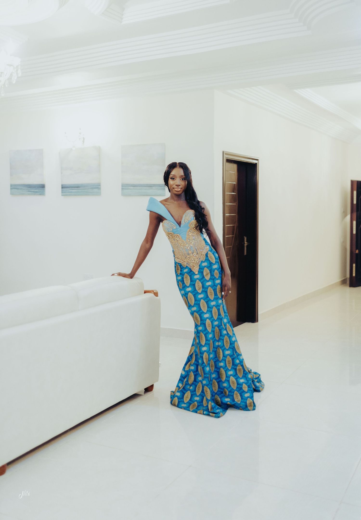 Floor-length blue and gold patterned dress with mermaid silhouette showcased in a minimalist white gallery.