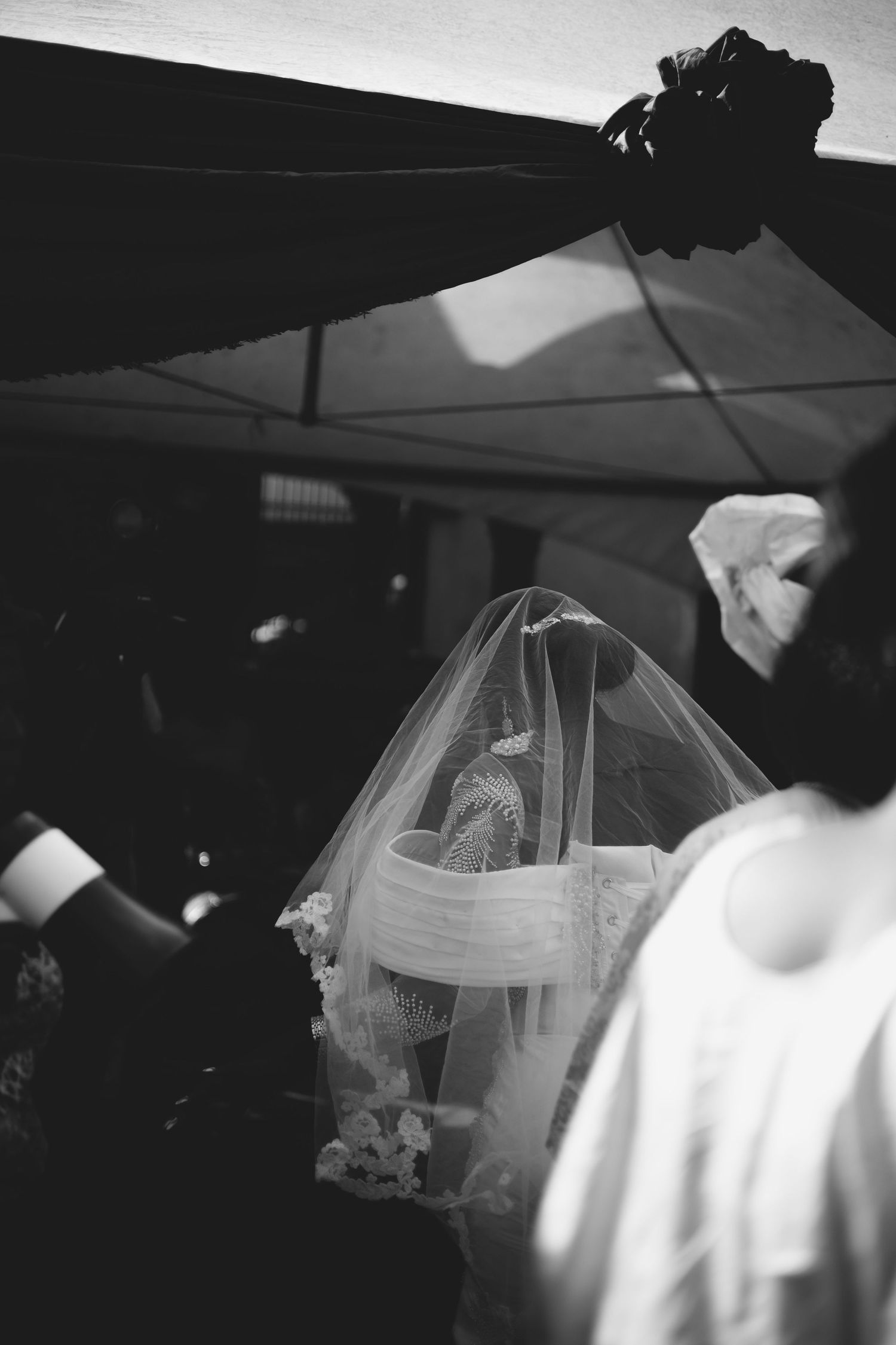 Black and white photo of a veiled bride during an outdoor wedding ceremony.