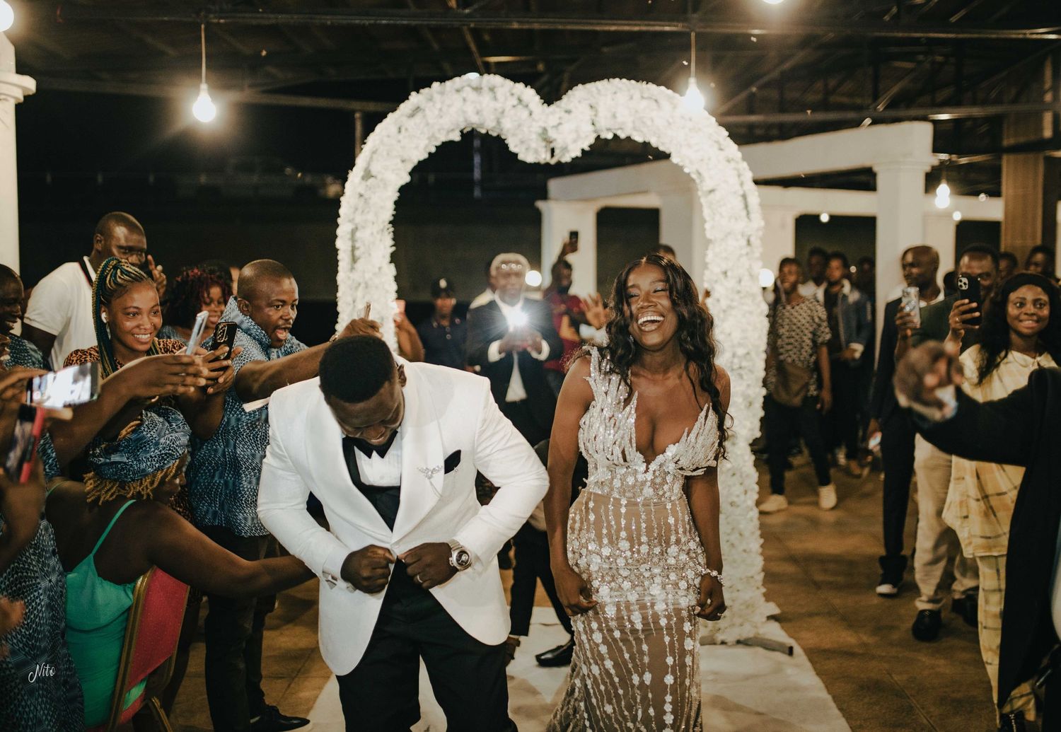 Couple dancing and celebrating under a white floral arch during their wedding reception.