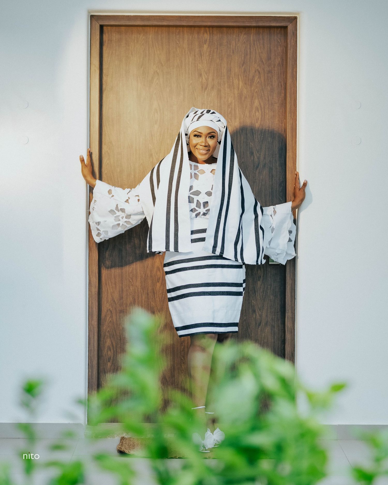 A figure in a white and black striped traditional garment poses in a doorway.
