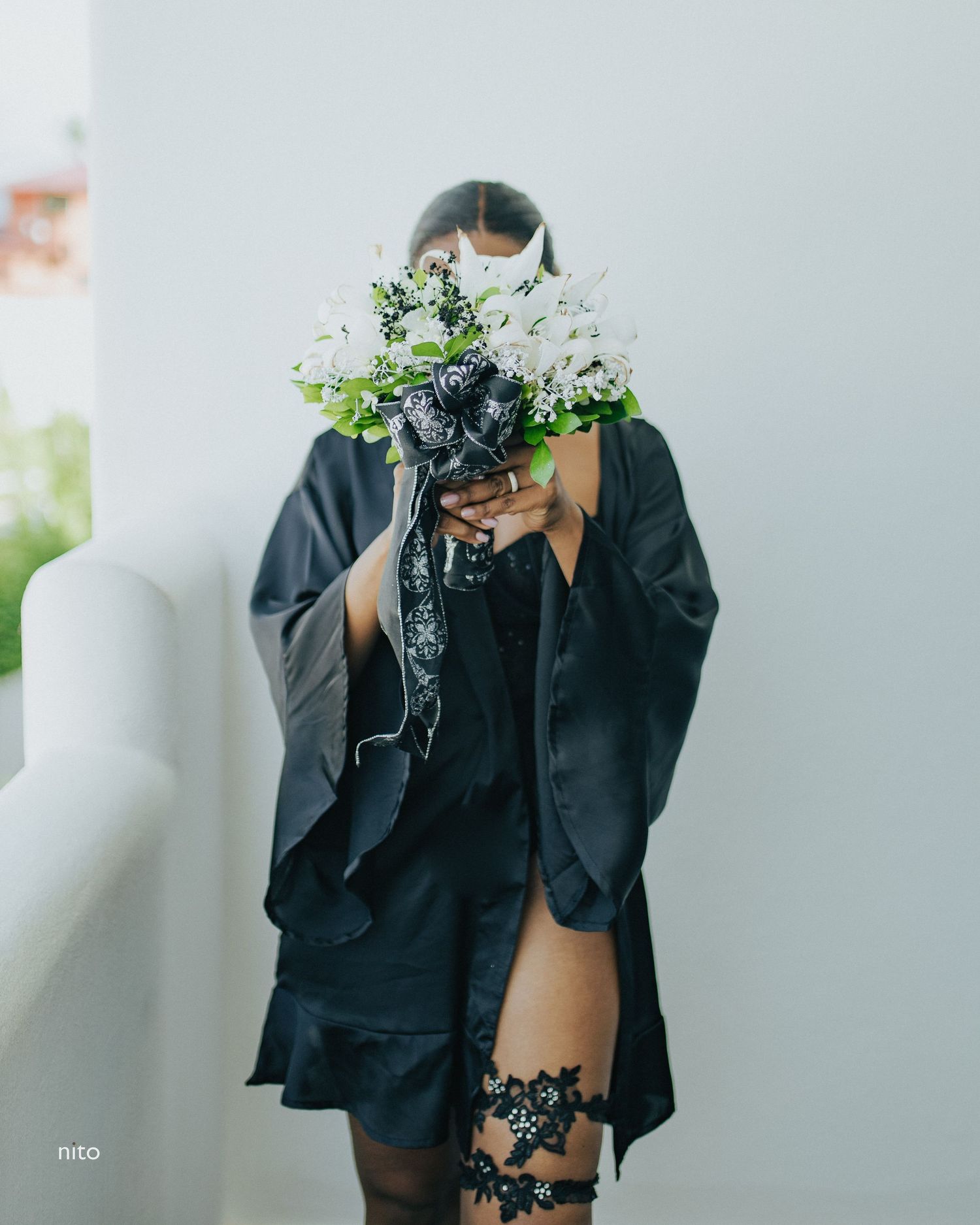 A figure in black holds a bouquet of white flowers covering their face.