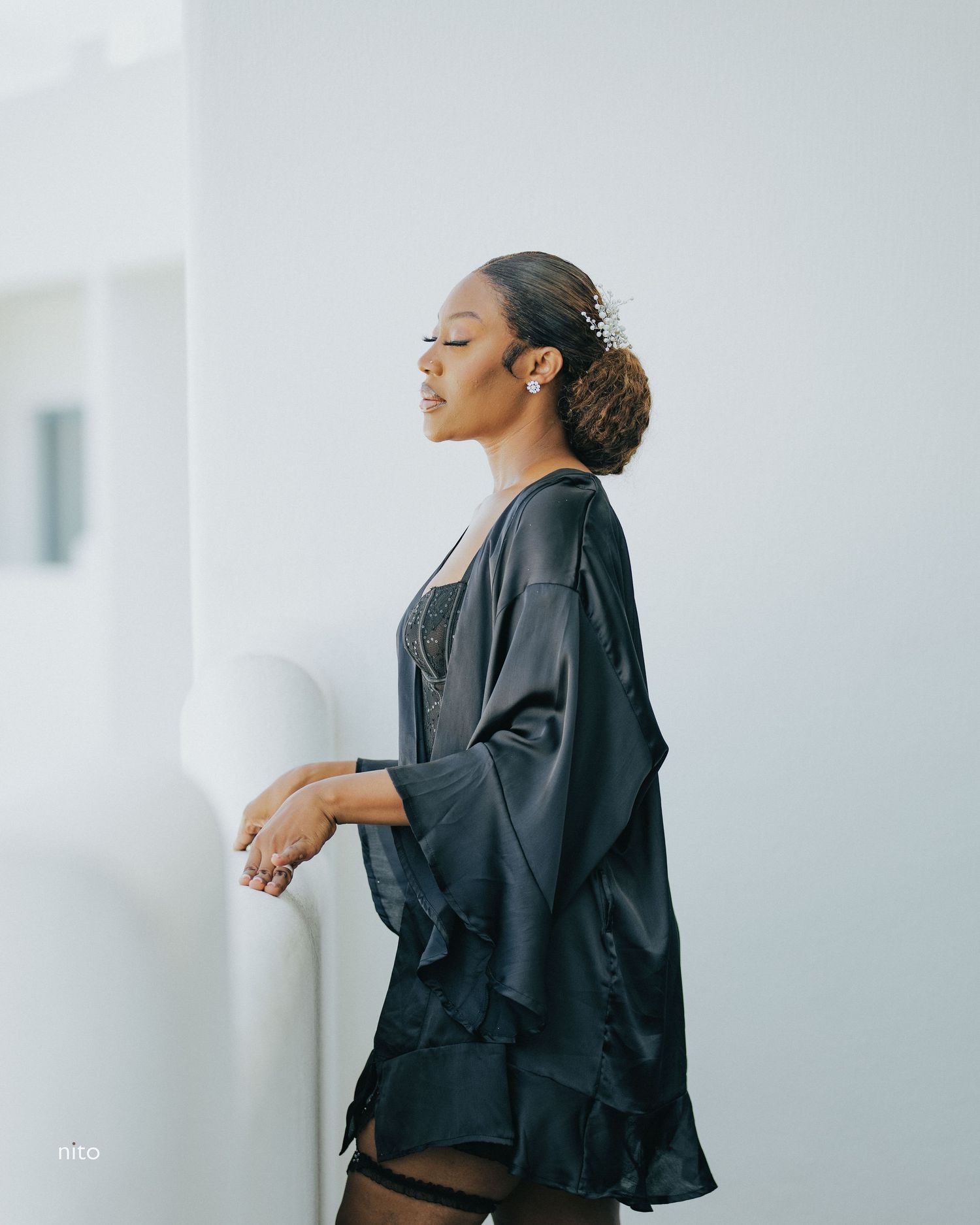 Side profile shot of model in flowing black silk robe against white wall.