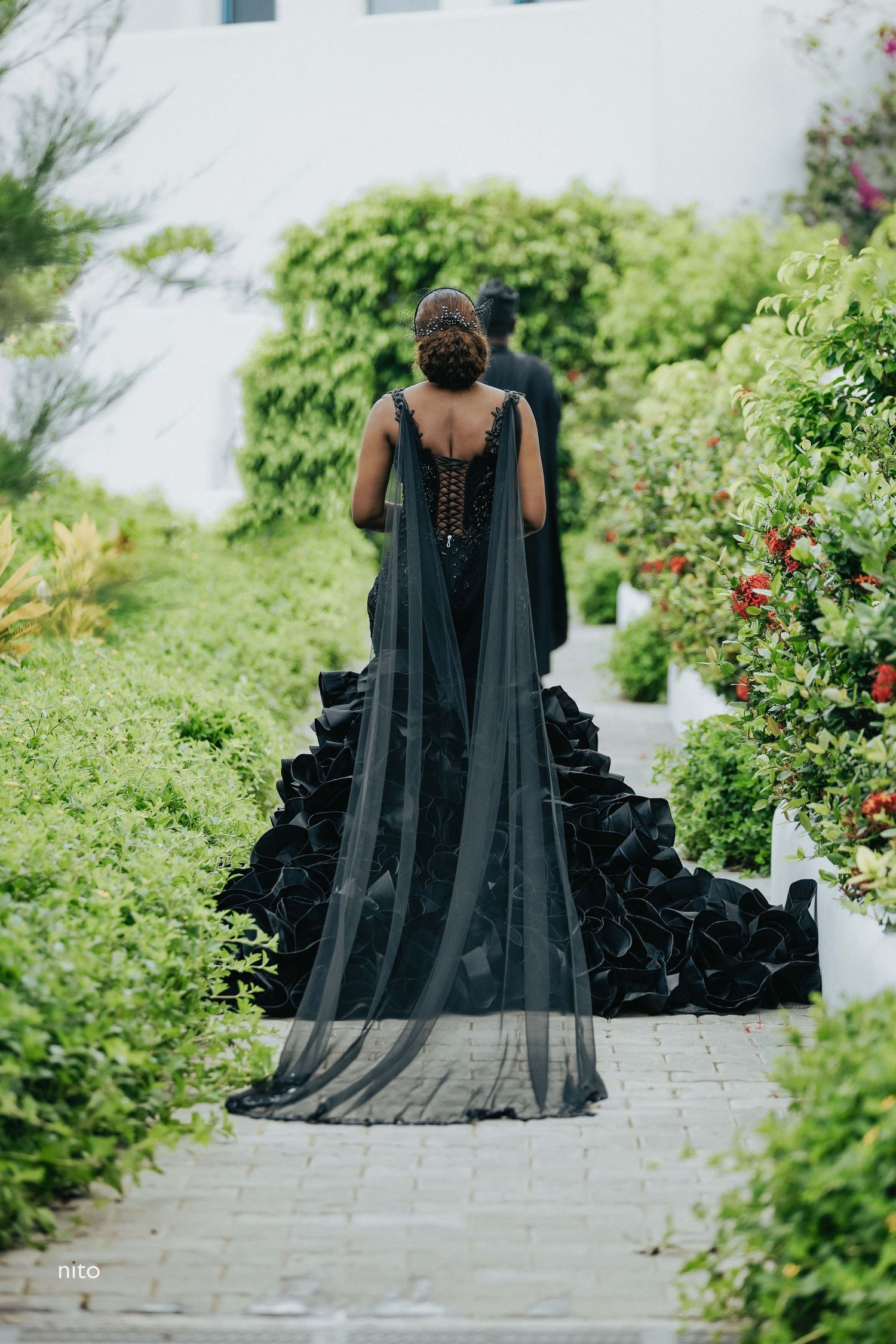 A dramatic black gown with flowing train photographed from behind in a garden setting.