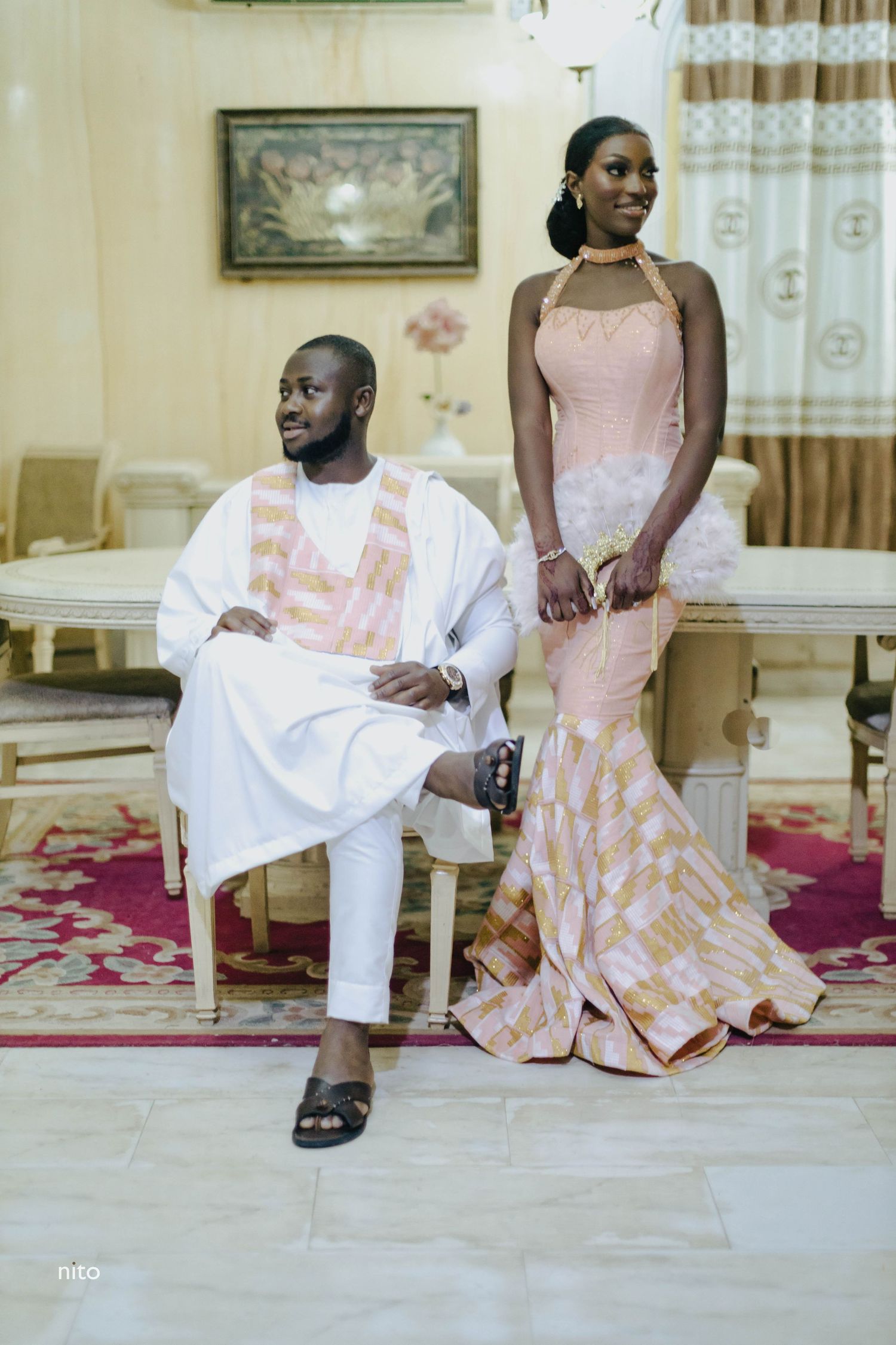 Formal couple in coordinated pink and white outfits posing in an elegant interior setting.