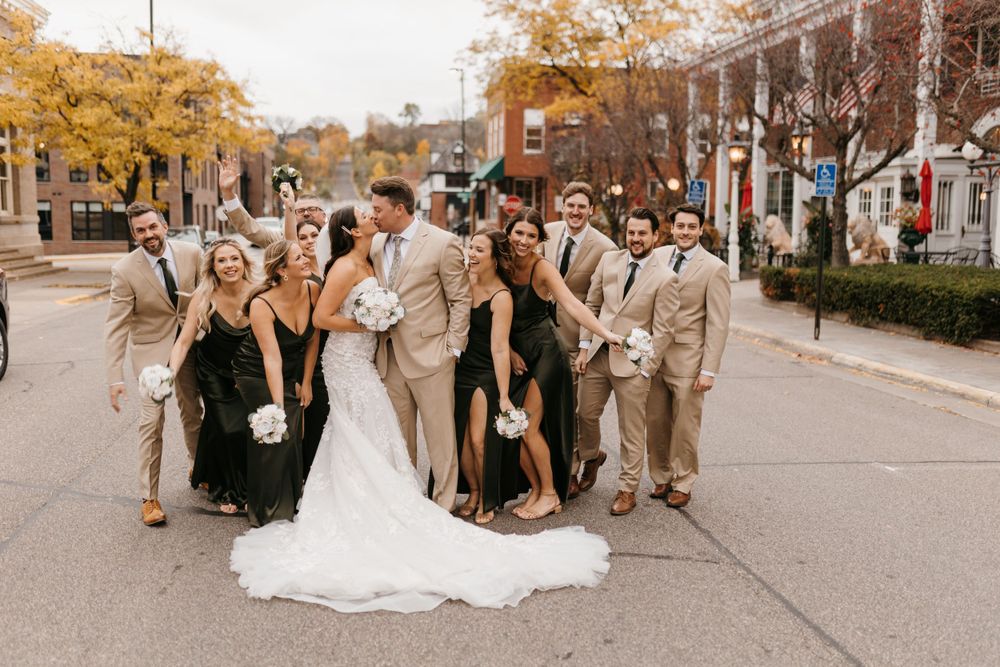 Fall wedding party poses on street, bridesmaids in black dresses and groomsmen in tan suits with bride and groom.
