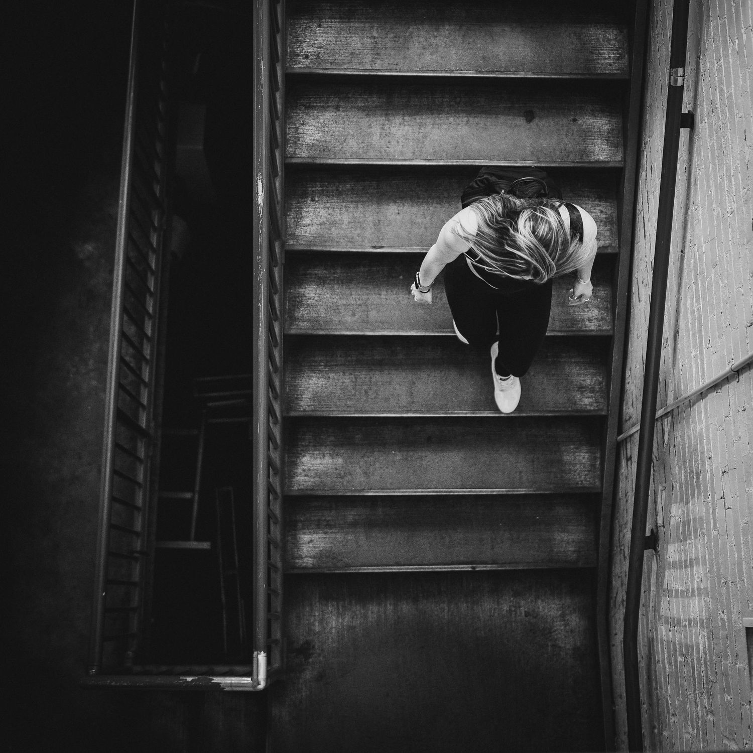 High angle view of person climbing dark wooden stairs in dramatic black and white.