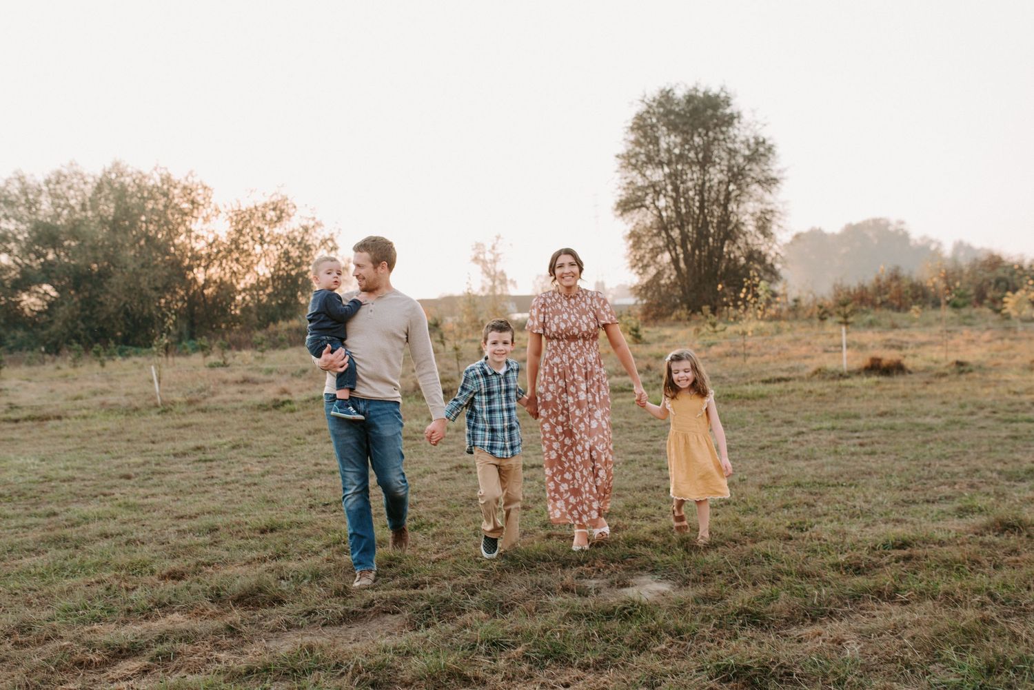 A family walking together in a golden field during sunset with mountains in the background.