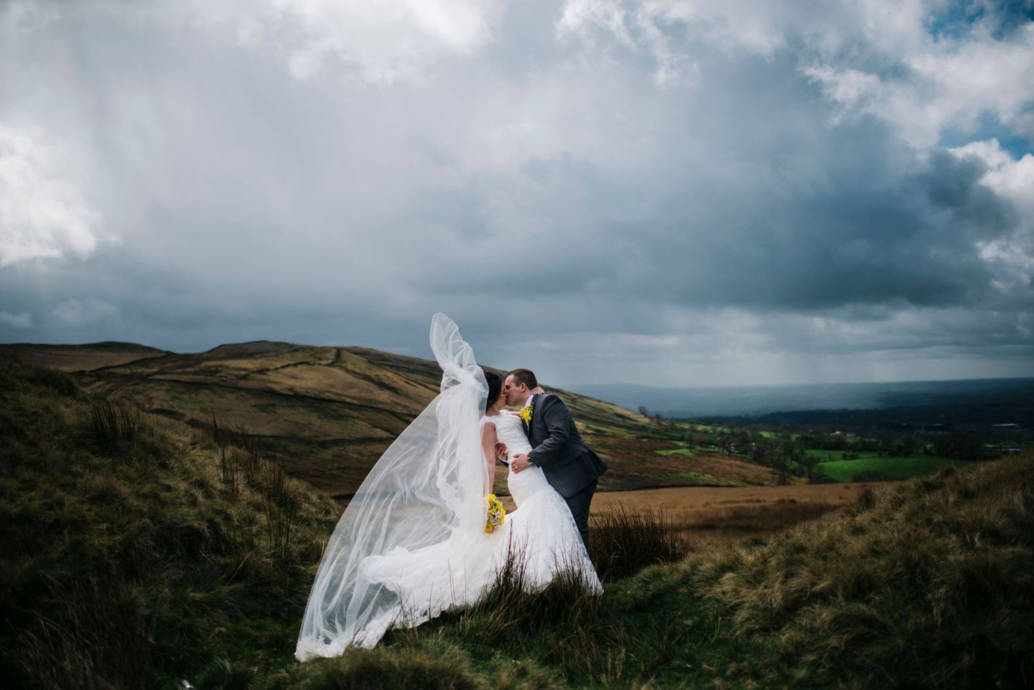 Dramatic wedding portraits against moody sky and rolling hills landscape.