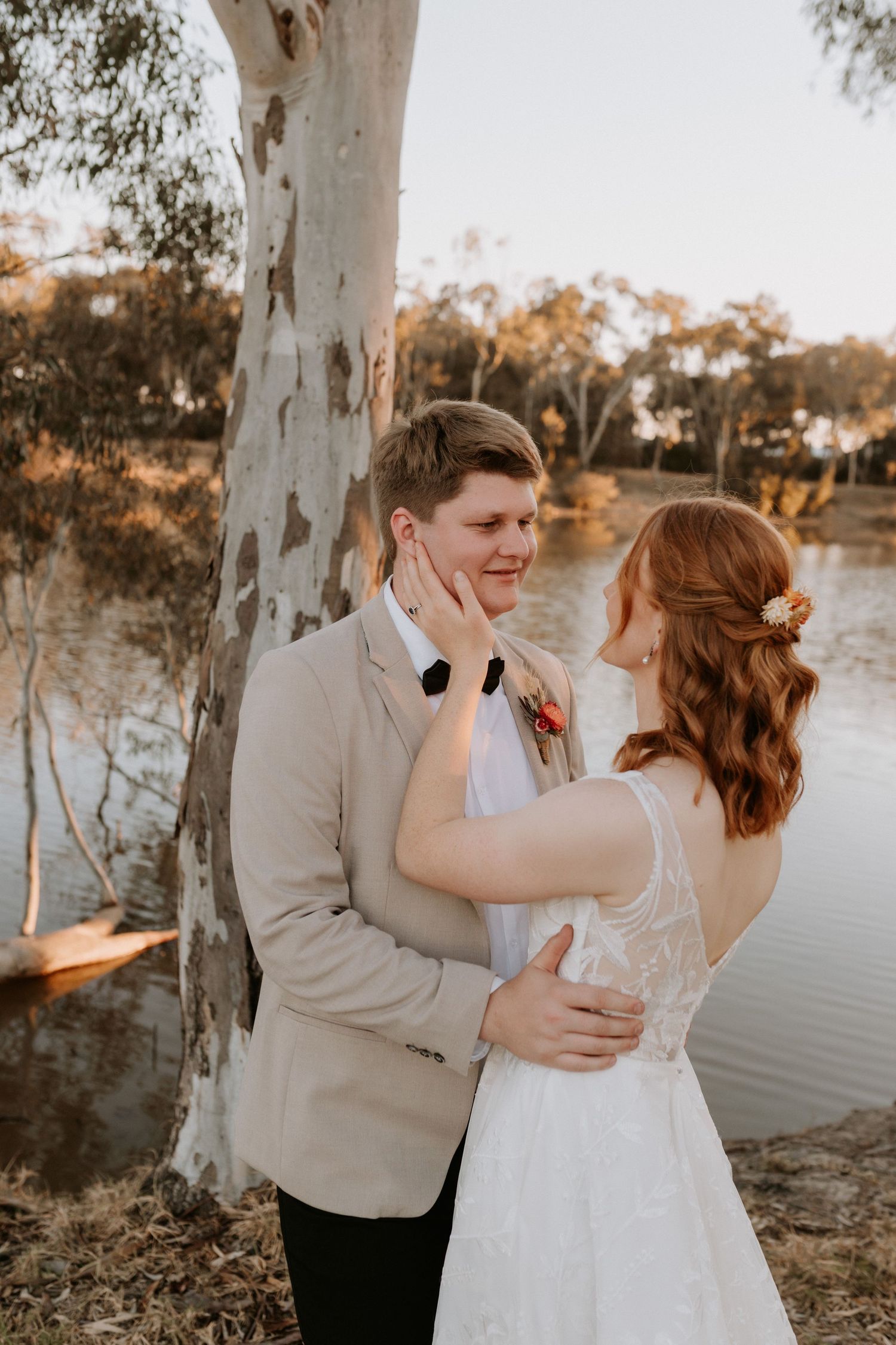 Tender moment between newlyweds by a river with eucalyptus tree during golden hour.